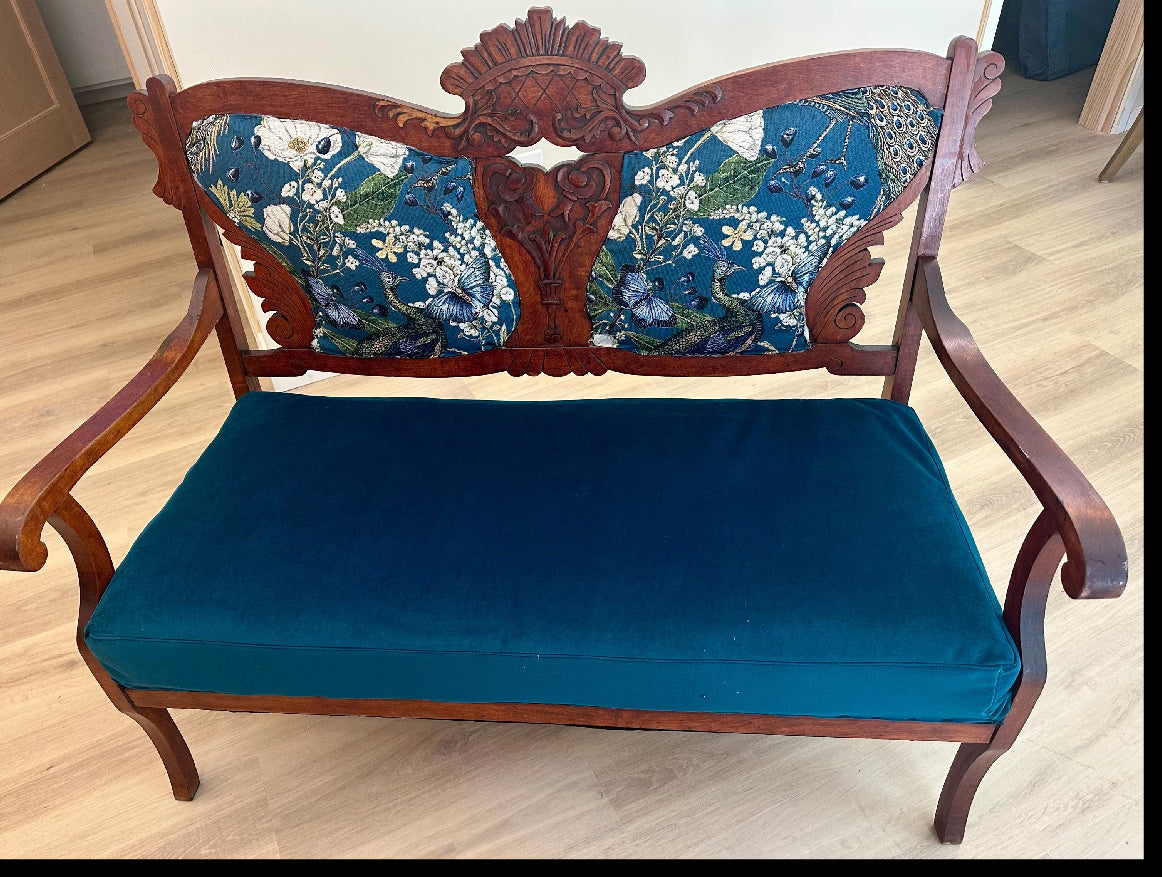 Wooden bench with floral-patterned backrest and blue cushion on a wooden floor.