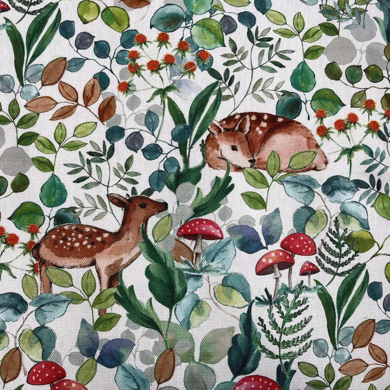 Whimsical woodland cotton fabric with deer, mushrooms, and forest leaves in green, teal, and red on a white background.