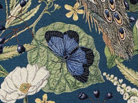 Thumbnail for Close-up of luxury tapestry fabric with intricate woven details showing a blue butterfly on a leaf, peacock feathers, and white flowers against a teal background.
