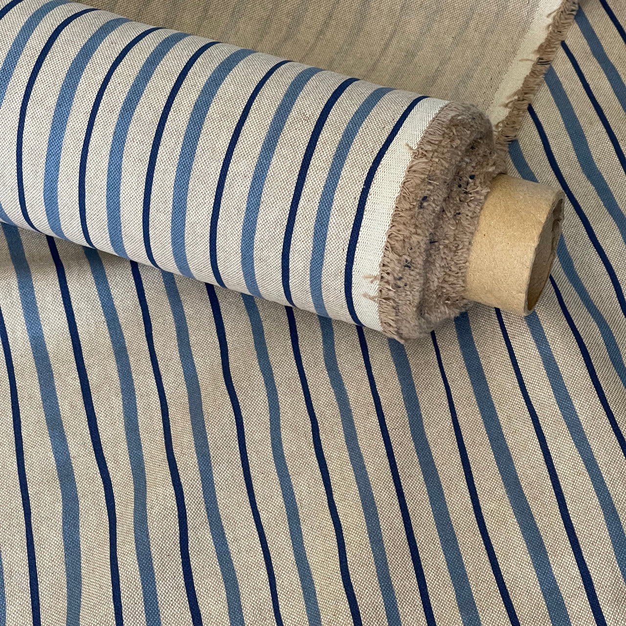 A close-up of striped fabric rolled on a cardboard spool, showing a woven beige base with vertical navy and medium blue stripes.