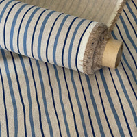 Thumbnail for A close-up of striped fabric rolled on a cardboard spool, showing a woven beige base with vertical navy and medium blue stripes.
