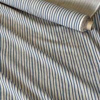 Thumbnail for A close-up of striped fabric with alternating vertical bands of blue, navy, and thin black lines on a warm beige background, with a rolled section showing the material texture and edge.