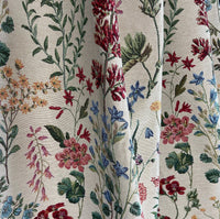 Thumbnail for Close-up of draped floral tapestry fabric with woven red, blue, and pink wildflowers on a cream background, showing soft texture and flow.