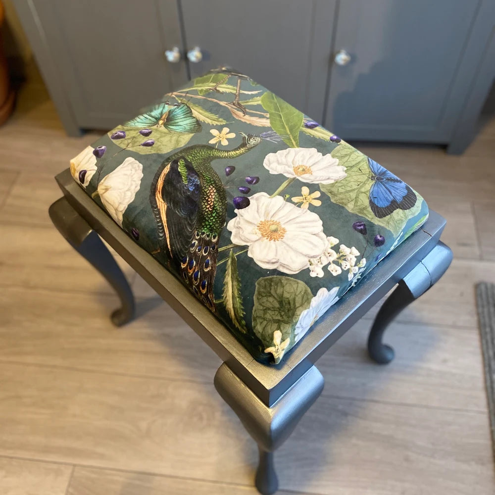 Decorative ottoman with floral and bird pattern on a wooden floor.