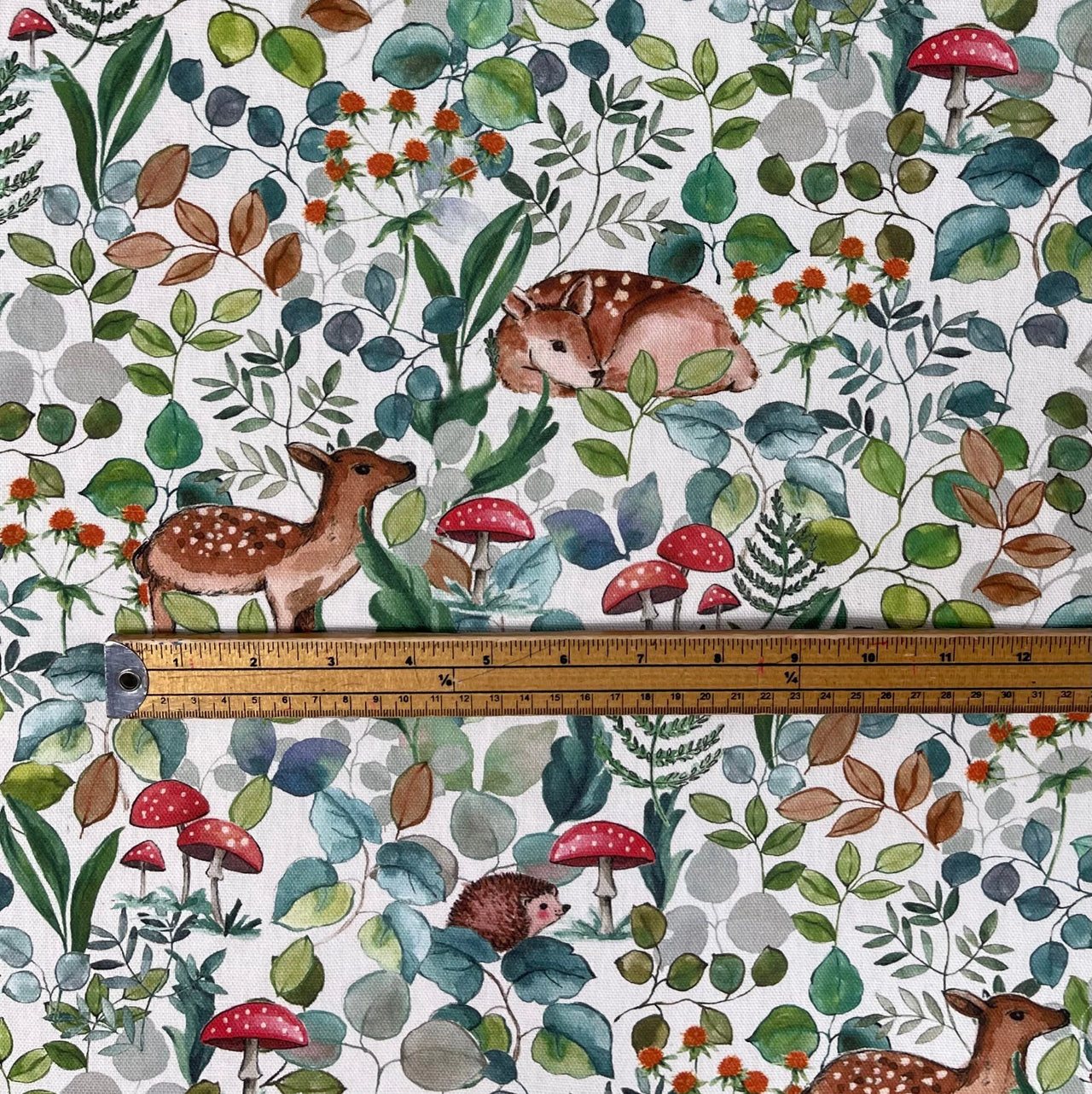 Printed woodland fabric with ruler showing scale – deer, hedgehogs, and foliage on white cotton. Great for upholstery or sewing.