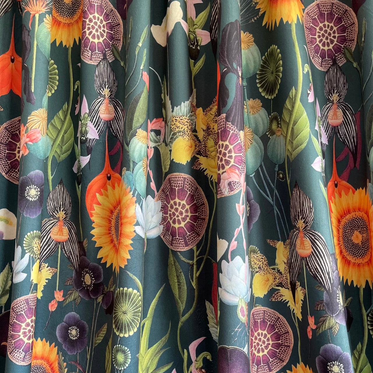 Botanical velvet fabric draped to show texture and movement, featuring a colorful floral print with sunflowers, poppies, and tropical foliage on dark green.

