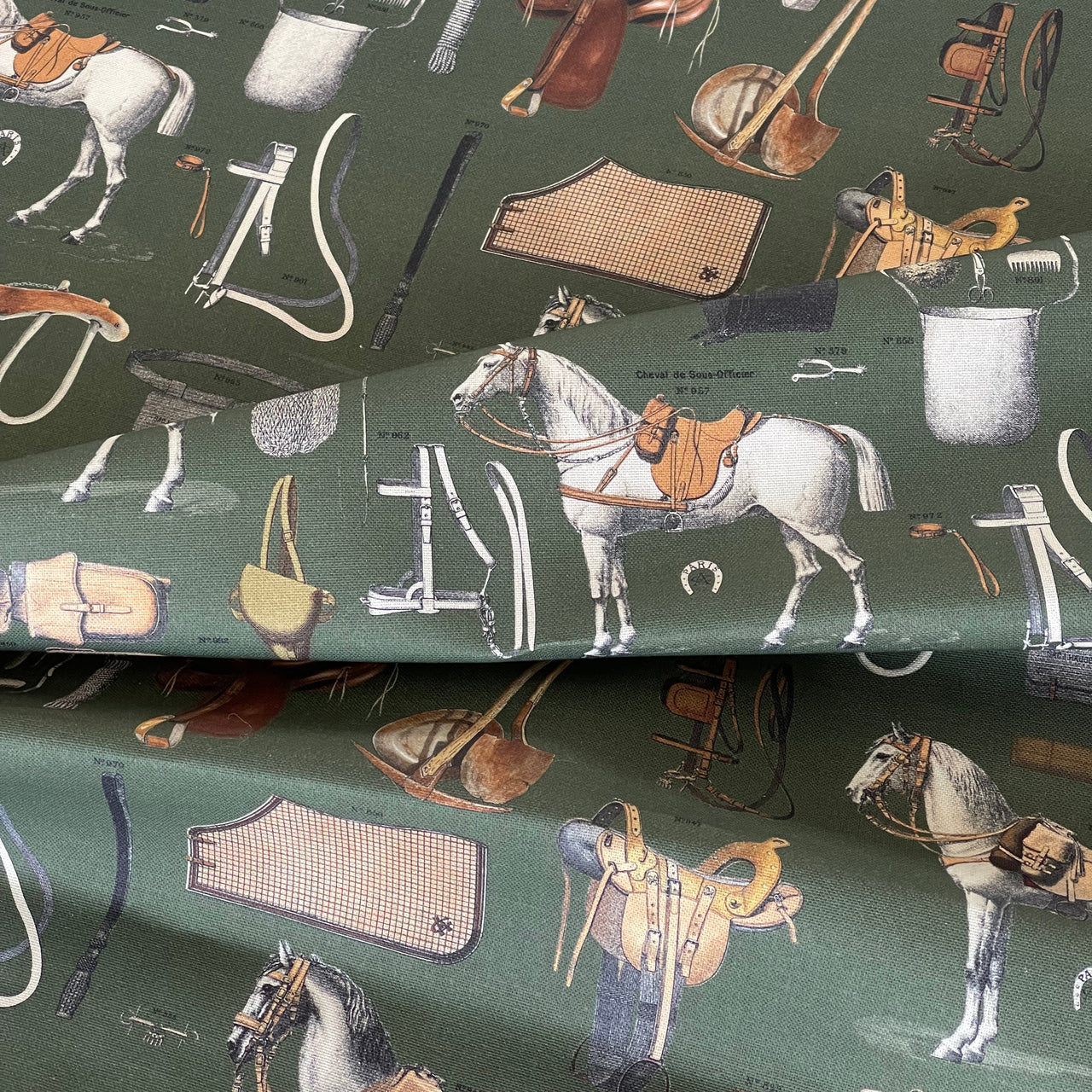 Fabric with equestrian-themed pattern featuring horses, saddles, and other tack on a green background.