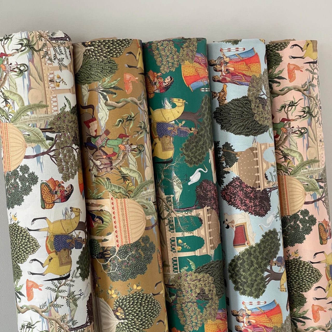 Five rolled fabrics featuring the Regalia Mughal pattern in various colorways including emerald, ochre, blush, and ivory.