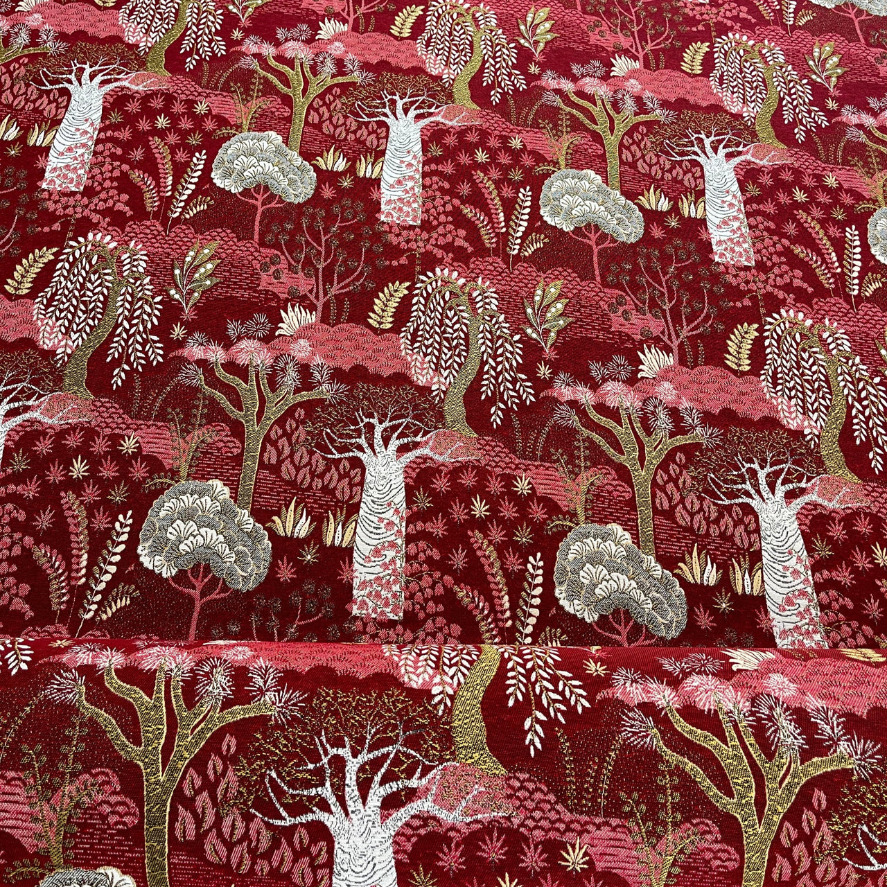Red fabric with a nature-themed pattern featuring trees and animals on a wooden surface.