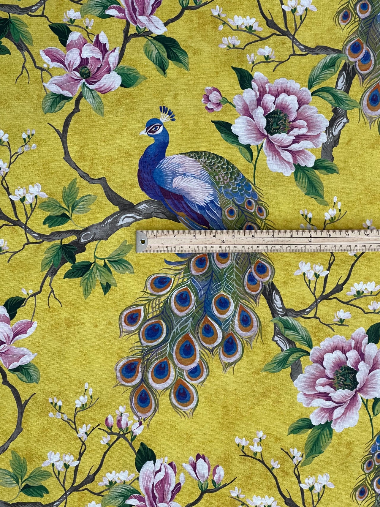 Fabric with peacock and floral design on a yellow background, measured with a ruler.