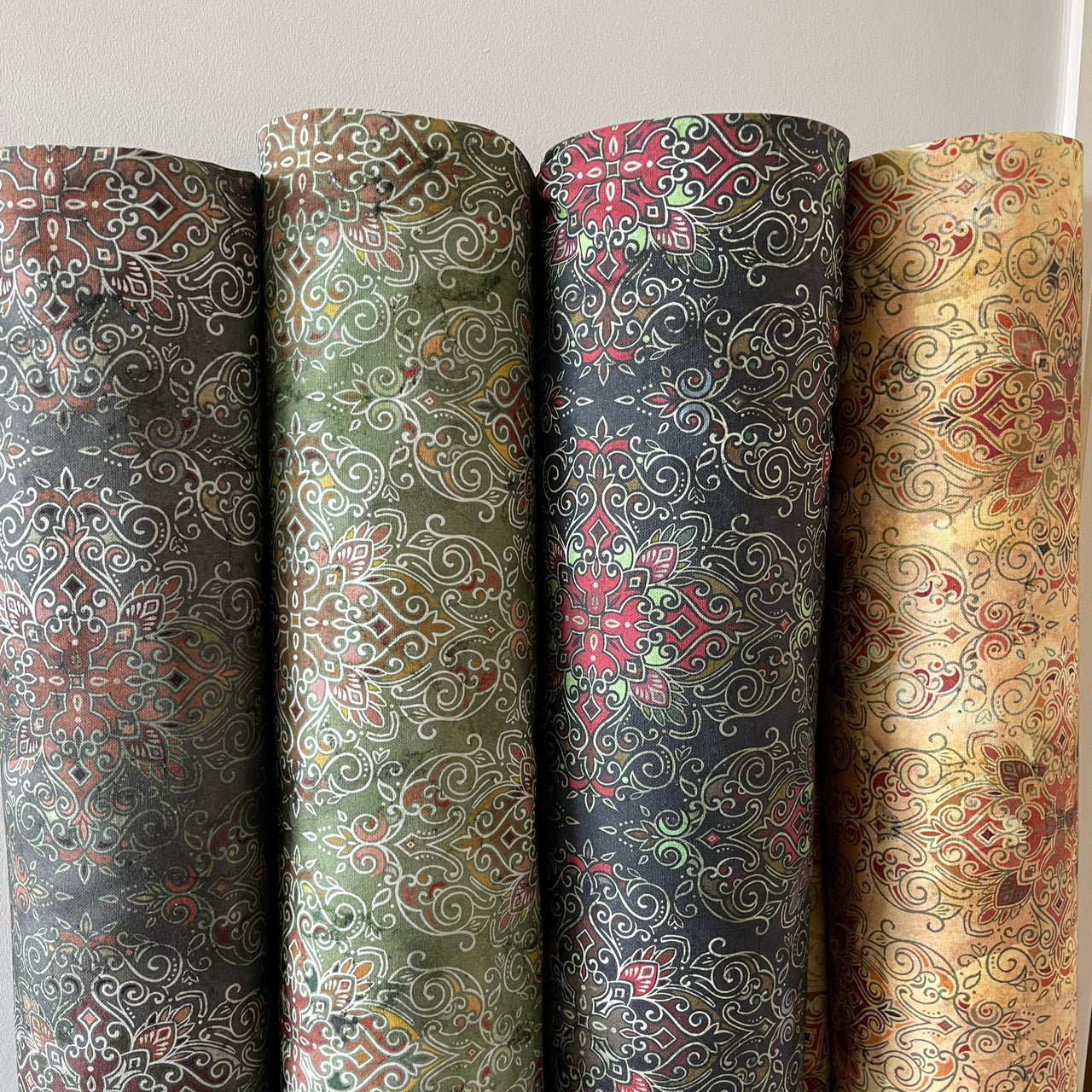 Four rolls of patterned fabric with different designs on a neutral background
