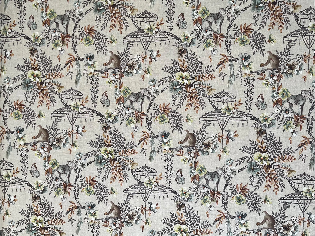 Flat lay of Savannah jungle print fabric featuring cheetahs, monkeys, parasols, and foliage on a beige linen-look background, perfect for safari-themed curtains and upholstery.