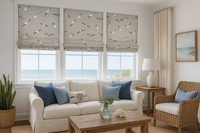 Thumbnail for A bright and airy coastal living room featuring seagull-patterned Roman blinds on two tall windows. The walls are painted a soft sandy beige. A cozy, off-white sectional sofa with seafoam and beige cushions sits opposite a natural driftwood coffee table. A navy throw blanket is draped casually over one arm. A jute rug covers the light wood floors. To the side, a painted white cabinet holds coastal décor: coral sculptures, sea glass vases, and nautical books. A large canvas of a lighthouse hangs above. Sunli