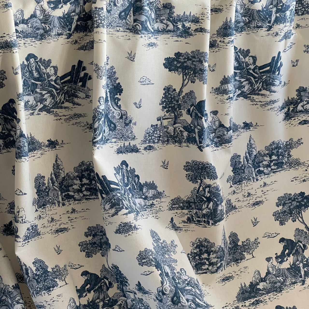 Blue and white toile patterned fabric with pastoral scenes.