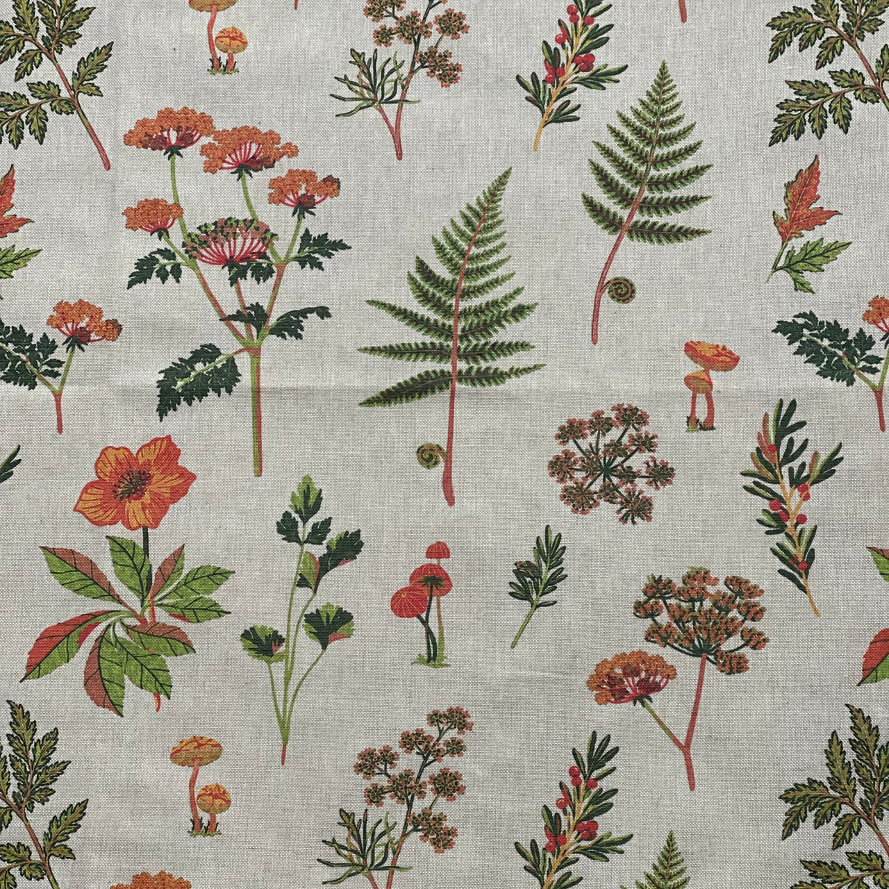 Close-up of small orange woodland mushrooms on pale grey botanical fabric with delicate green foliage.
