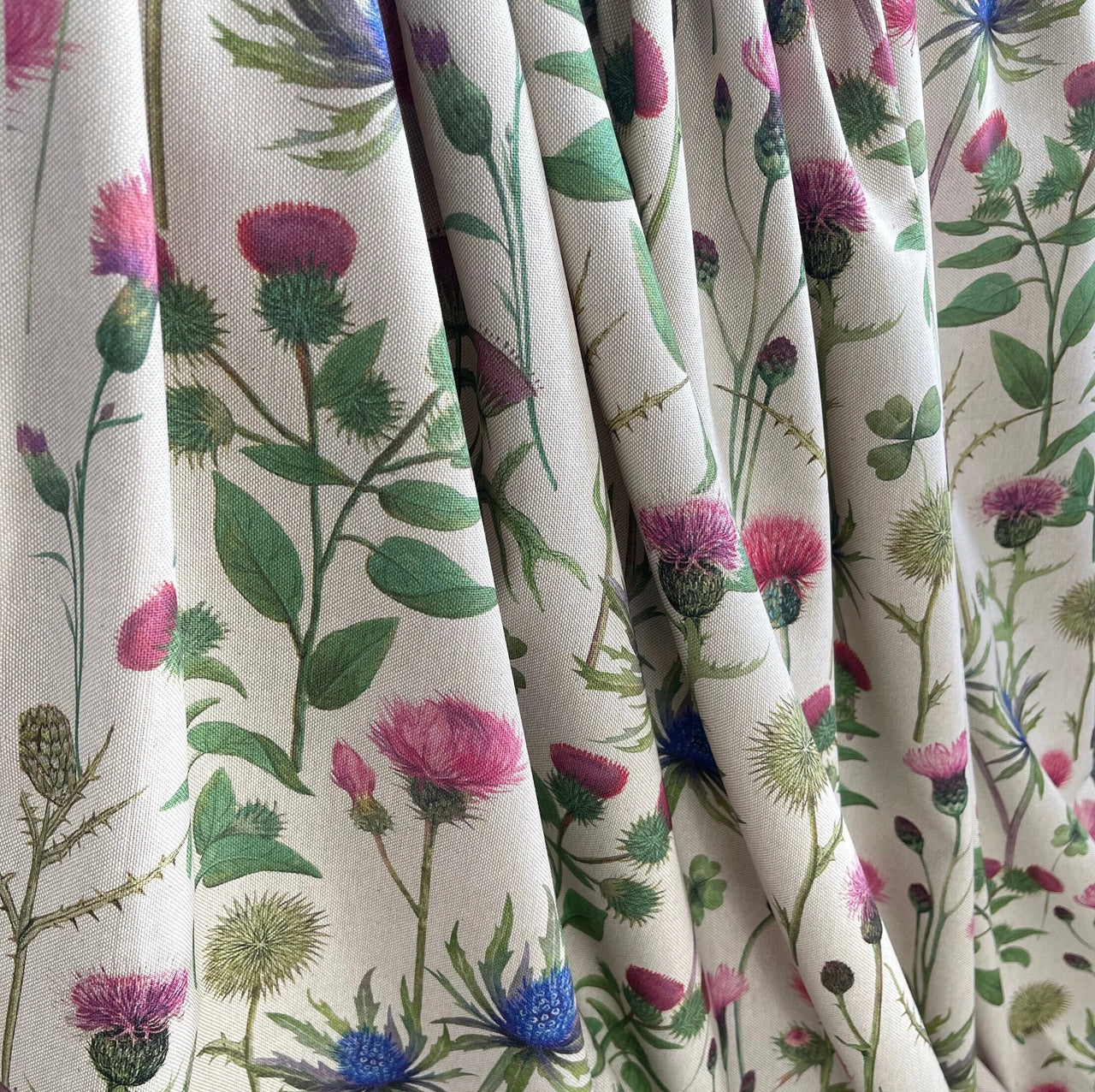Draped cotton-linen fabric with botanical Scottish thistle and eryngium print in pink, blue, and green on a neutral background.