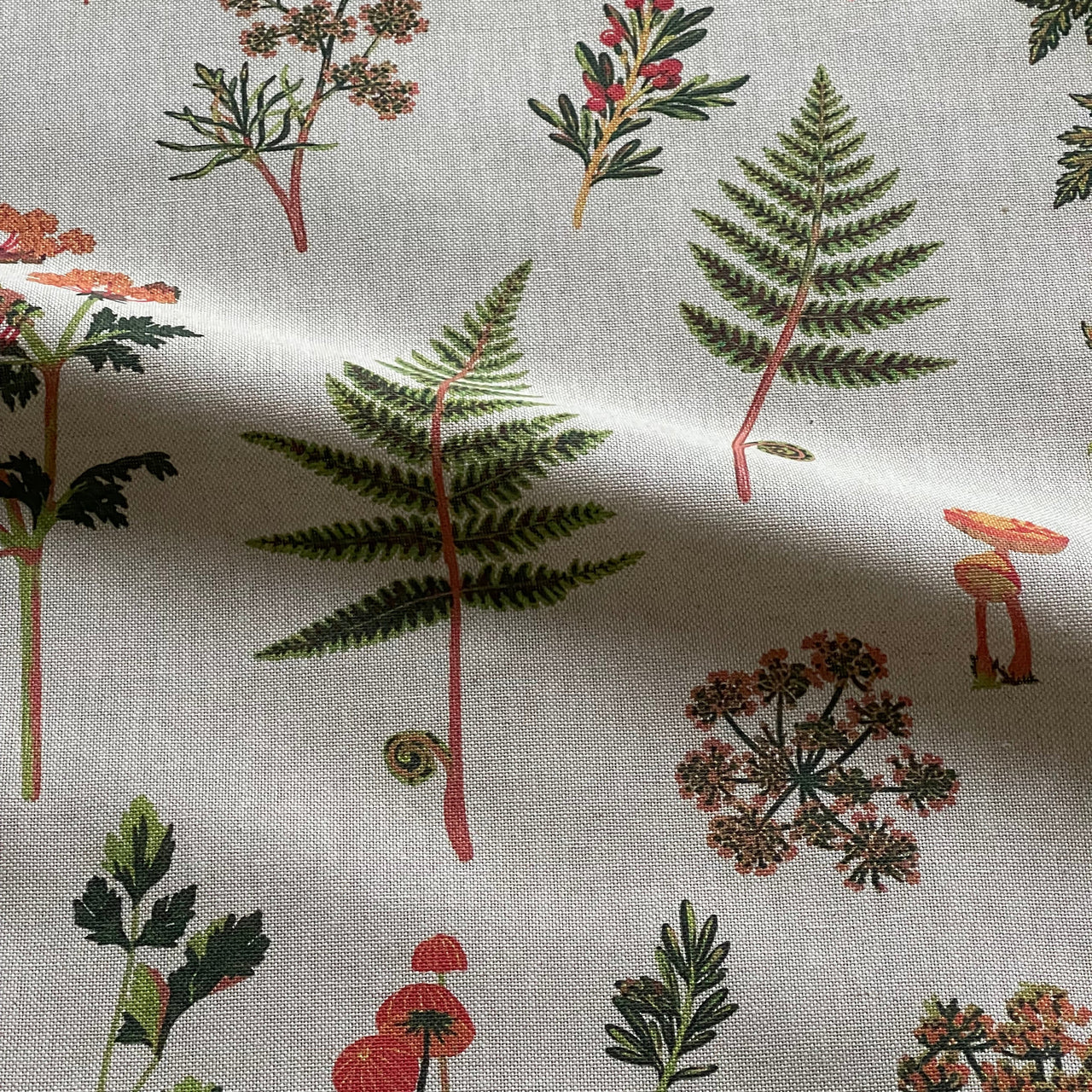 Close-up of medium-weight botanical furnishing fabric showing its woven texture and printed green and orange woodland design.