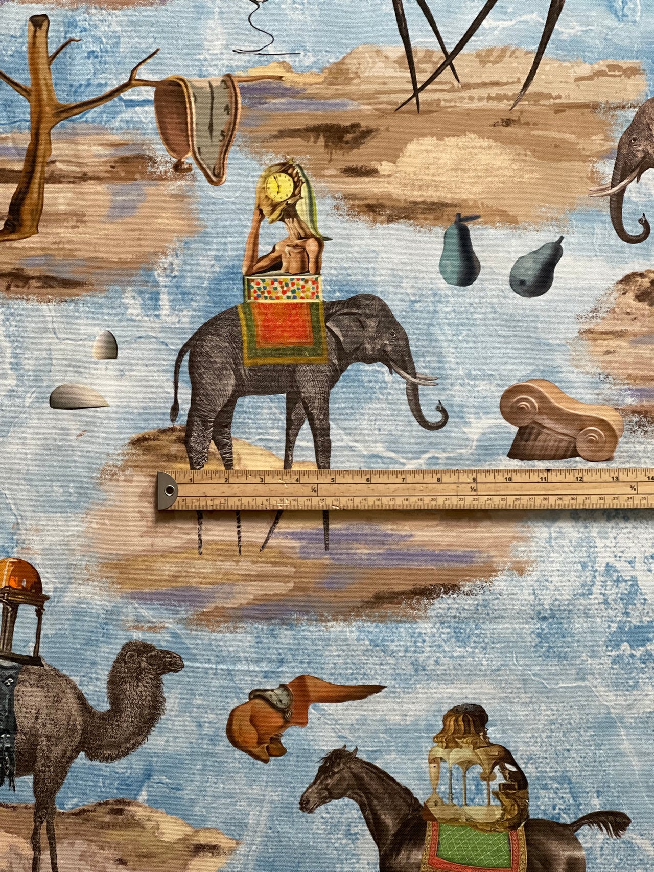 Wide photograph of blue artistic cotton furnishing fabric with elephants, camels, horses and whimsical surrealist landscape elements.