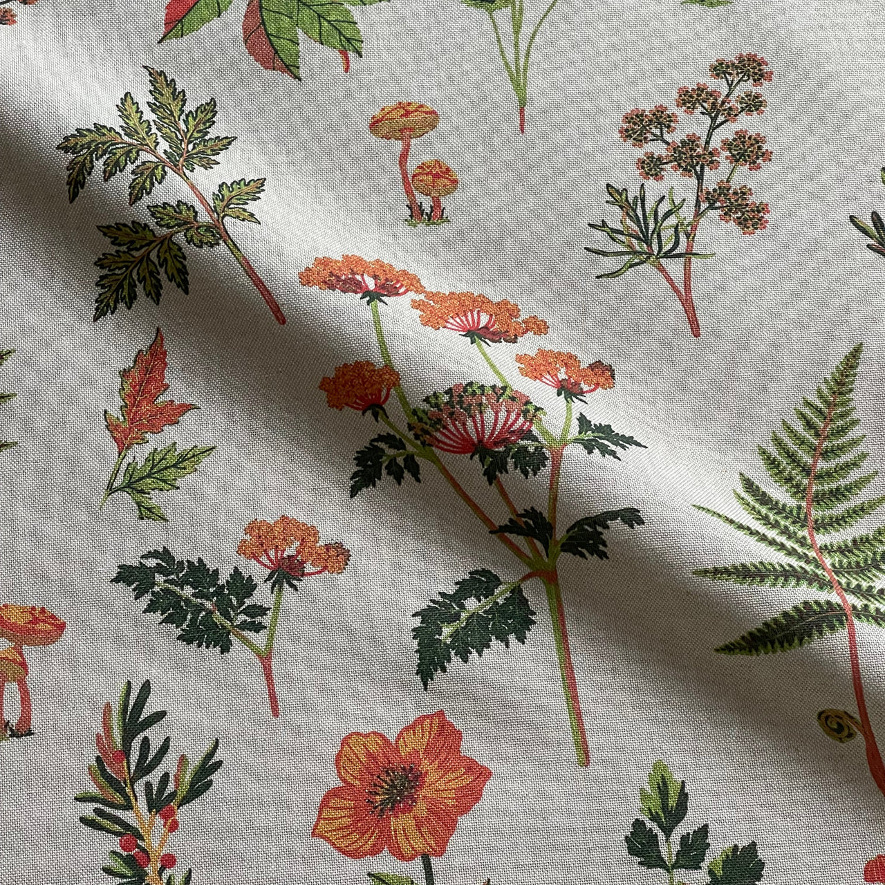 Full view of grey woodland botanical fabric featuring green ferns, orange wildflowers, mushrooms and delicate leafy sprigs