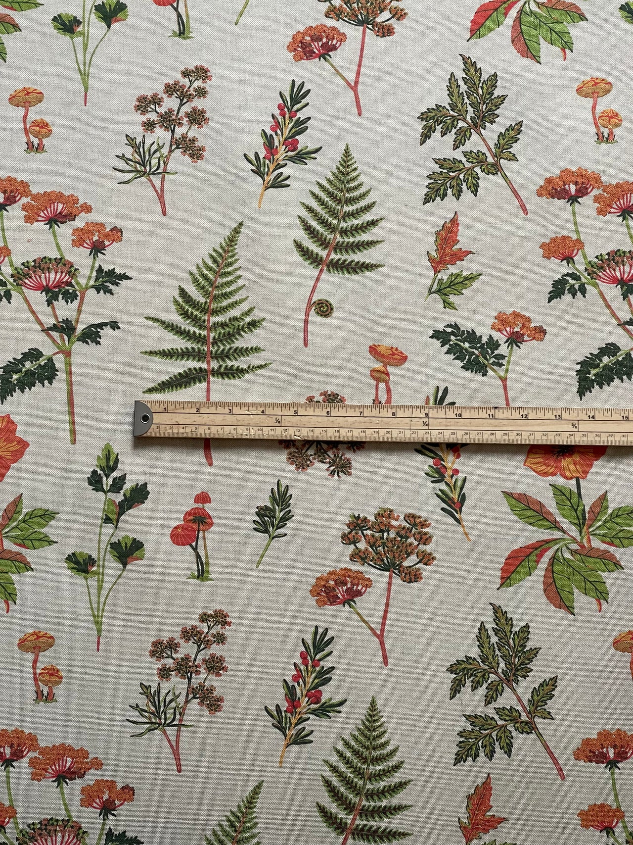 Close-up of woodland floral fabric showing detailed orange blossoms, green leaves and fine botanical illustrations.